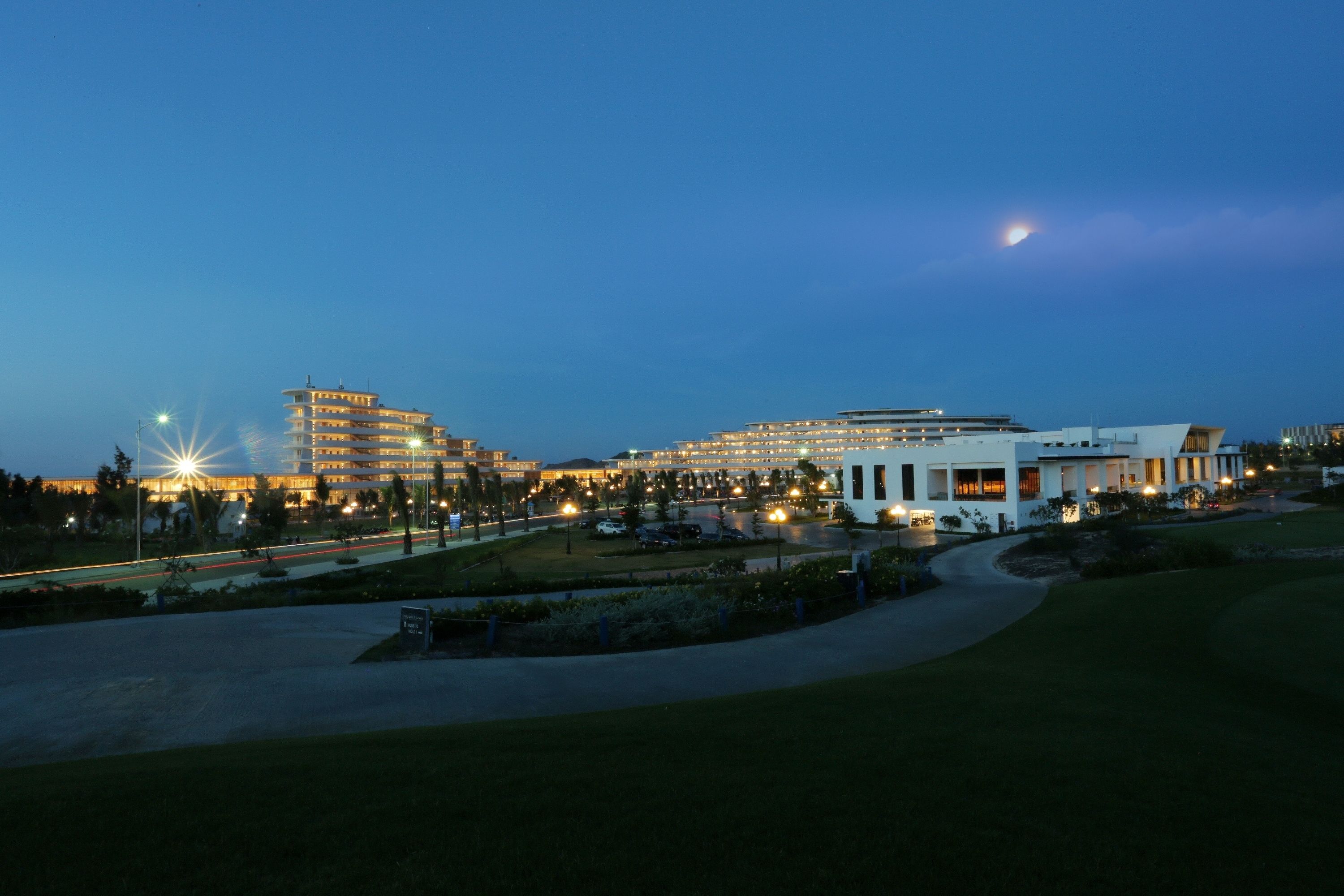 A hotel complex with multiple buildings, a parking area, and well-lit pathways.