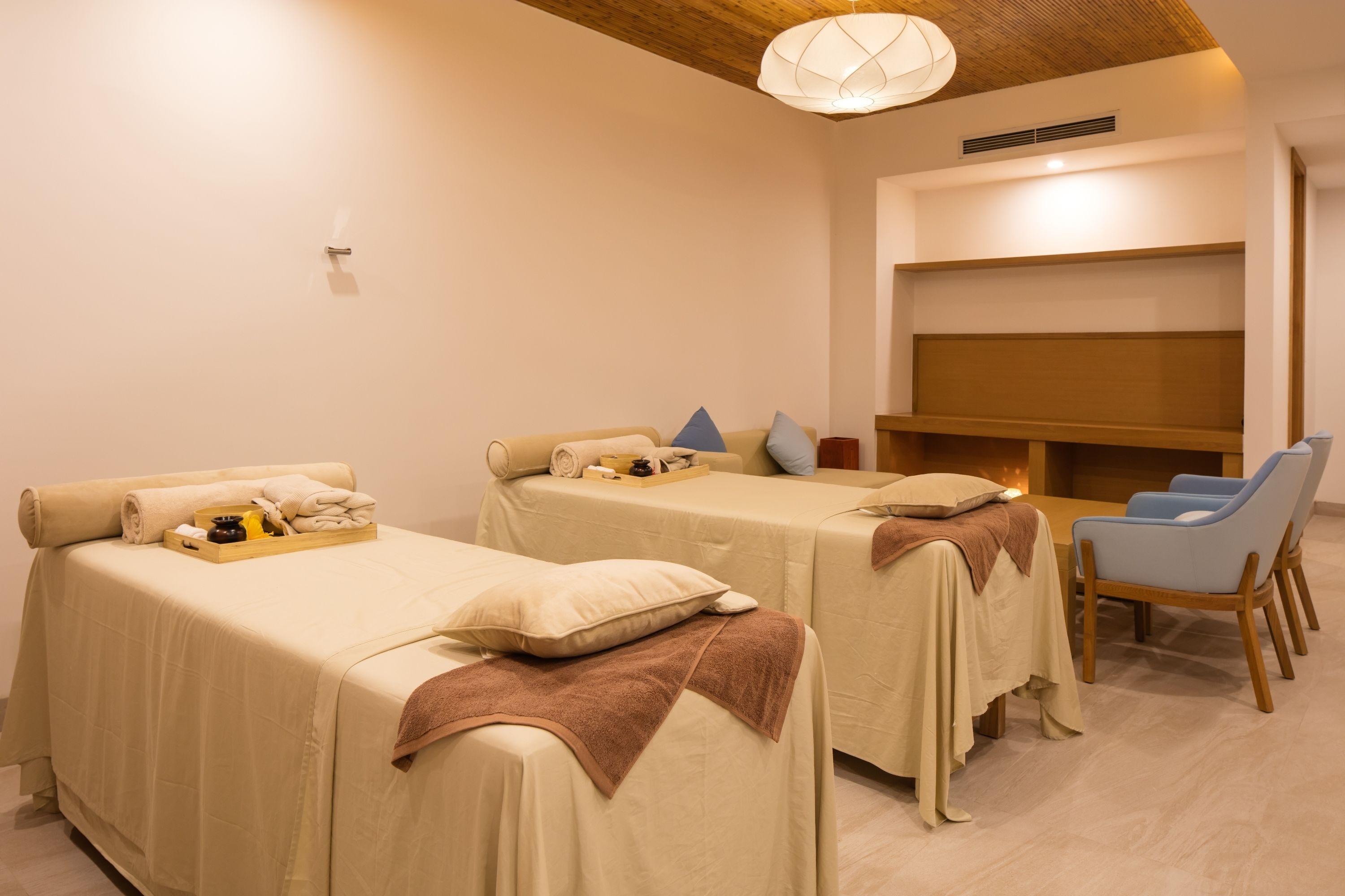 A room with two beds, a seating area with chairs, and a wall-mounted shelf.