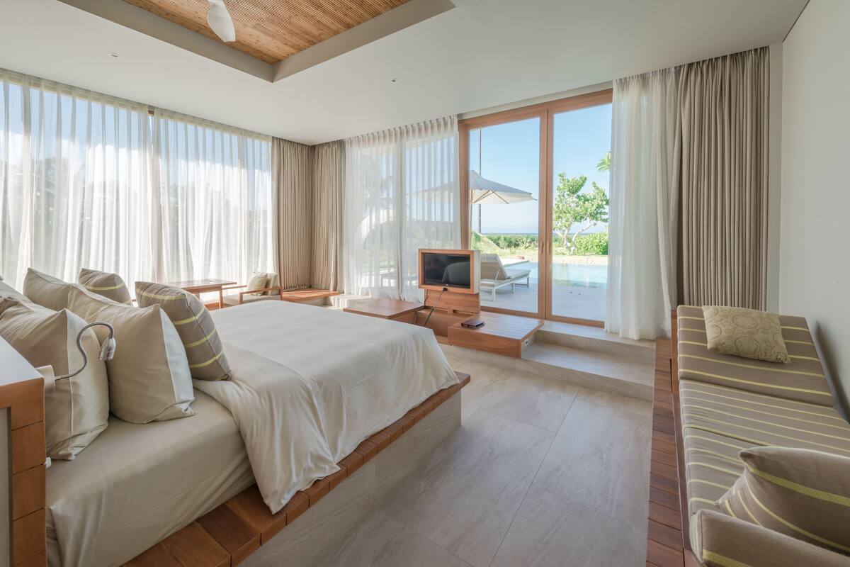 Une chambre d’hôtel moderne dotée d’un grand lit, d’un canapé, d’une télévision et d’un balcon offrant une vue sur la mer.