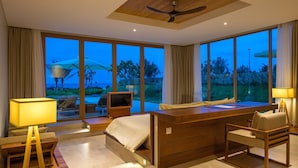 Une chambre d’hôtel moderne dotée d’un grand lit, d’un bureau et d’une télévision. La chambre dispose de grandes fenêtres offrant une vue sur l’océan et les palmiers.