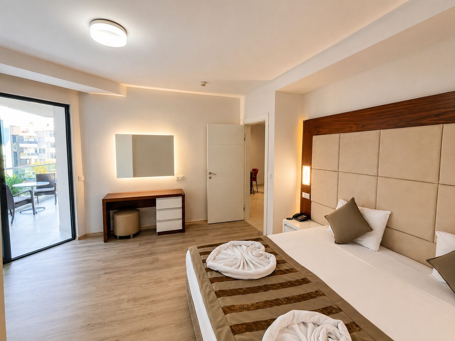 A hotel room with a bed, bedside table, desk, chair, and a view of the outside.