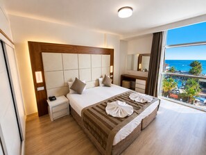Hotellihuone, jossa on suuri sänky, yöpöytä, peili ja näkymä merelle.