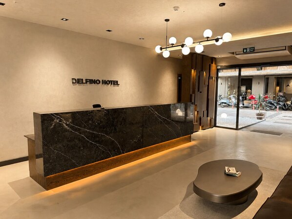 A hotel reception desk with a marble counter, a wooden base, and a modern light fixture above.