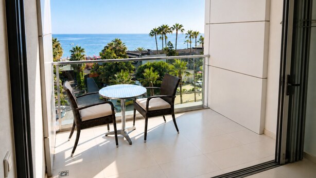 Ein Balkon mit Tisch und Stühlen, der Blick auf einen Strand mit Palmen und den Ozean bietet.