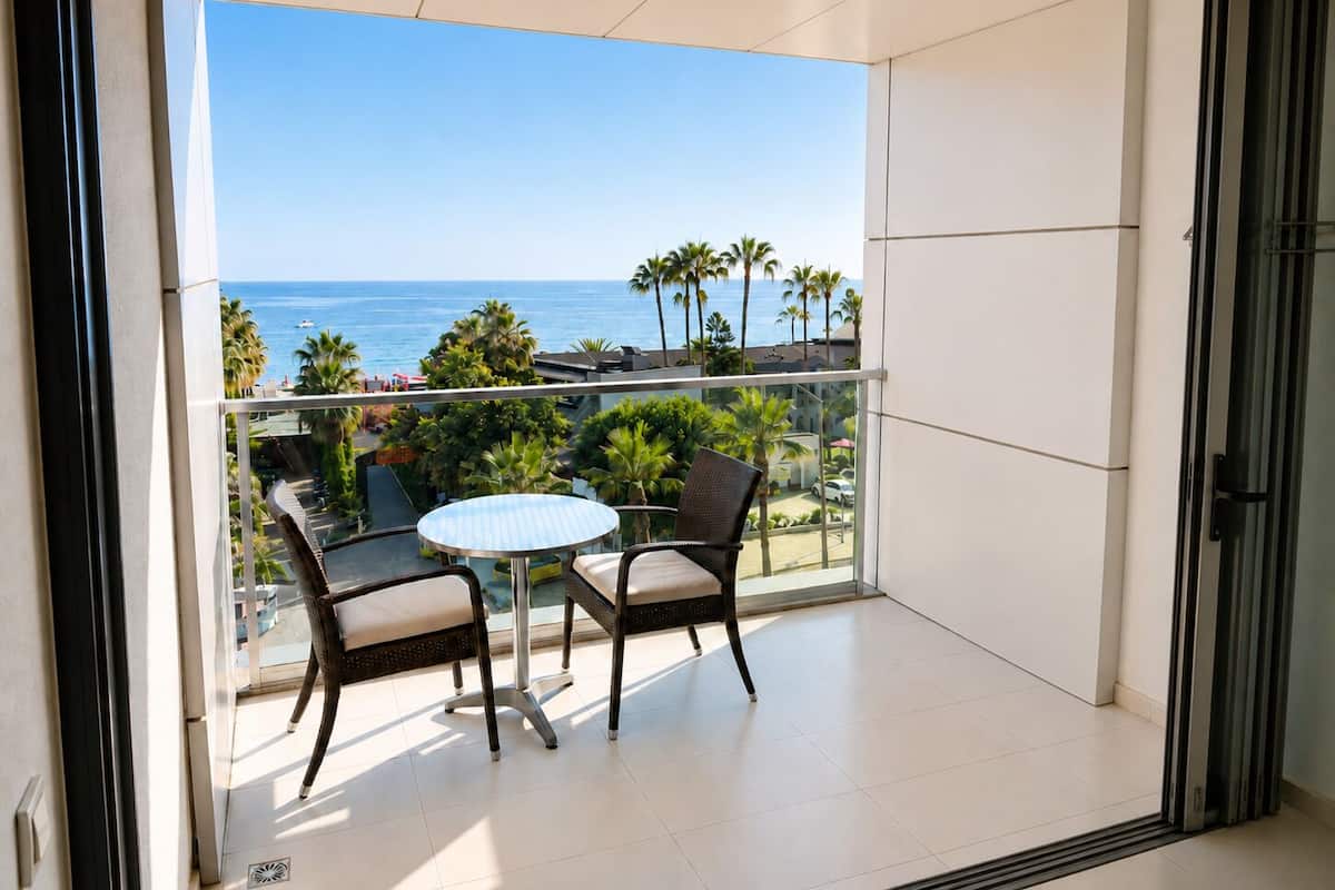 Un balcon avec une table et des chaises, donnant sur une plage bordée de palmiers et sur l’océan.