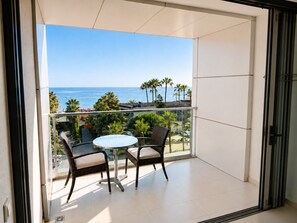 A balcony with a table and chairs, overlooking a beach with palm trees and the ocean.