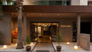 Der Eingang des Delfino Hotels mit modernem Design, eine Glasfassade, ein einladender Innenbereich mit Sitzgelegenheiten und ein gut beleuchteter Weg zum Eingang.