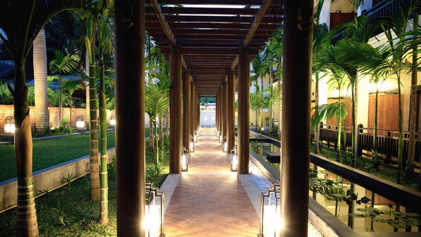 A covered walkway with columns, palm trees, and a water feature.