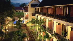 A hotel with multiple floors, a swimming pool, and palm trees.