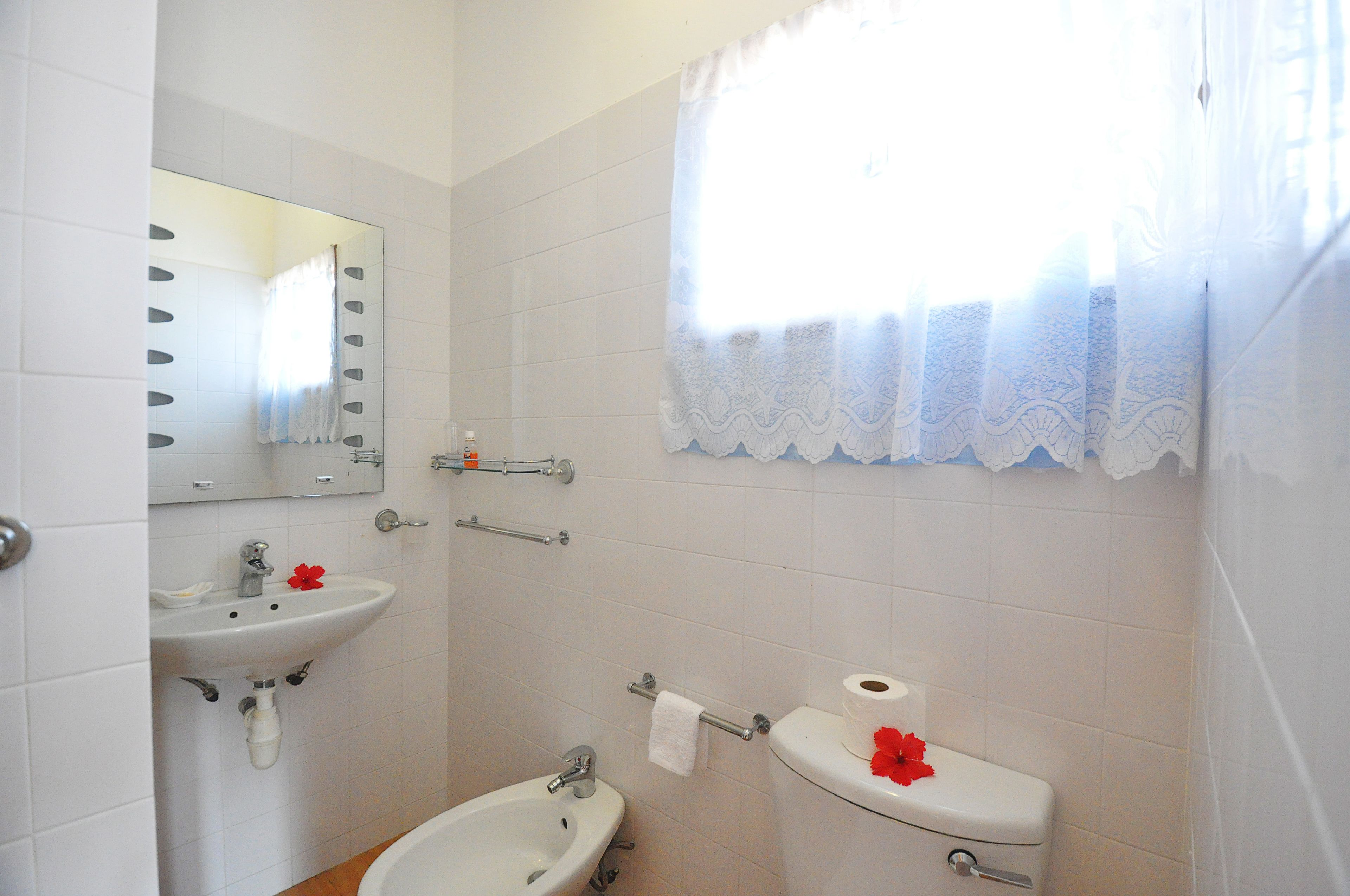 Un baño con lavamanos, espejo, inodoro y ventana con cortinas de encaje.