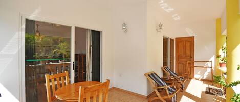 A spacious balcony with a sliding glass door leading to a garden, wooden furniture, and a yellow accent wall.