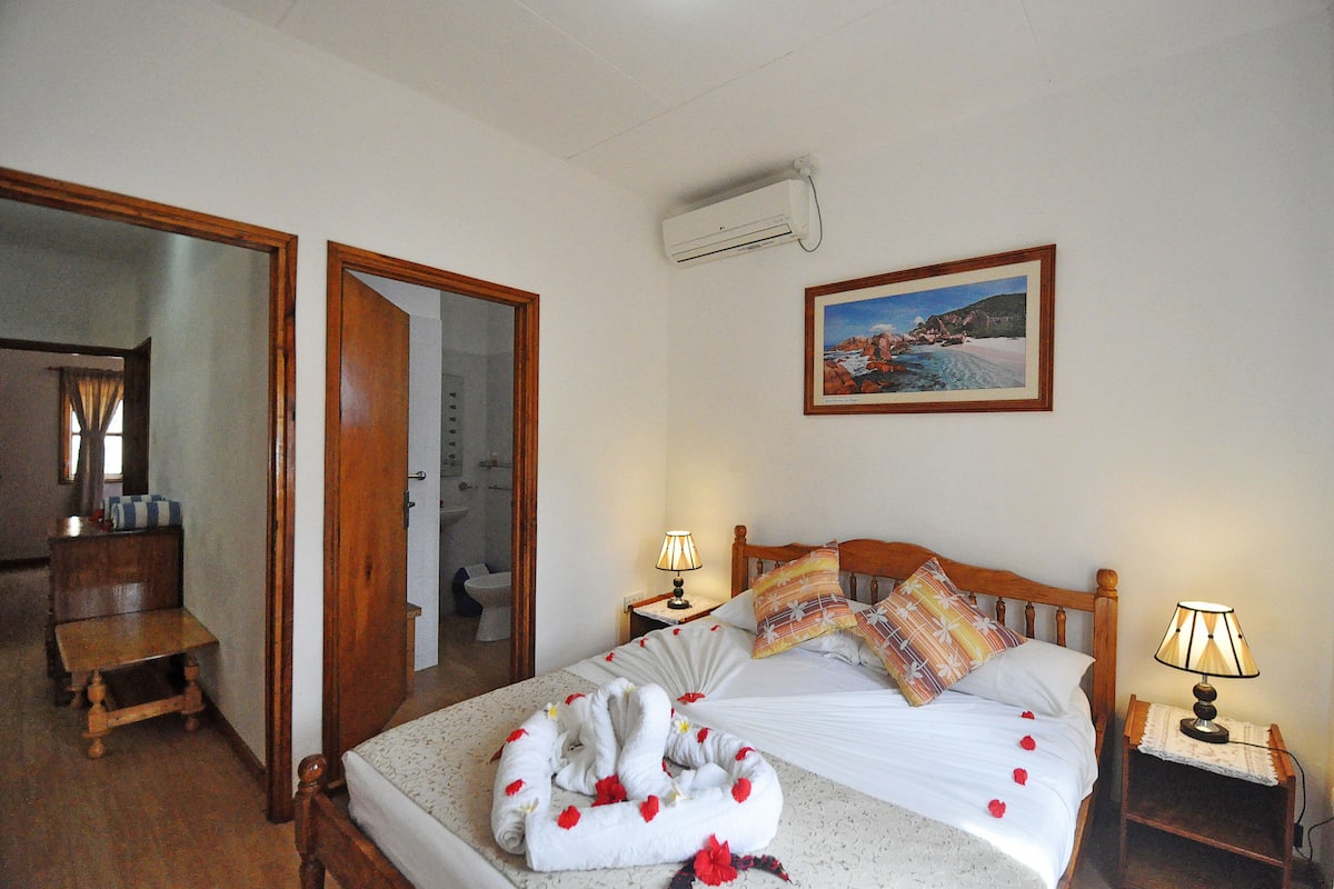 Ein Hotelzimmer mit einem Bett, Nachttischlampen, einem Gemälde und einer Klimaanlage.