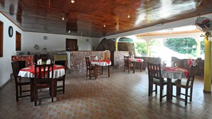 A restaurant with a rustic interior, featuring wooden tables and chairs, a stone counter, and a view of greenery outside. - Acquario Villa (Praslin Island)