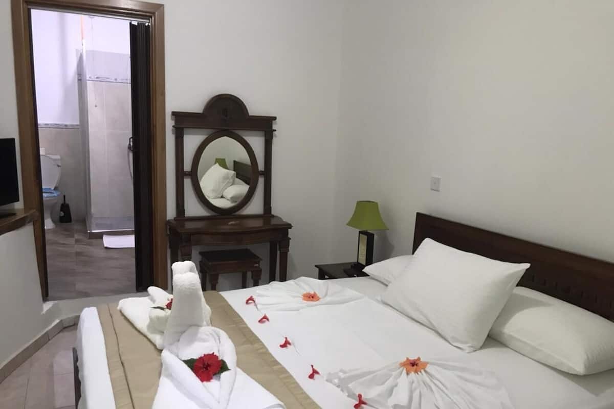 Ein Hotelzimmer mit einem Bett, einem Nachttisch, einem Spiegel und einem durch eine geöffnete Tür einsehbaren Badezimmer.