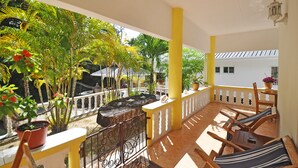 A balcony with yellow pillars, a wrought iron railing, and a view of a garden with various plants and a white building in the background. - Acquario Villa (Praslin Island)