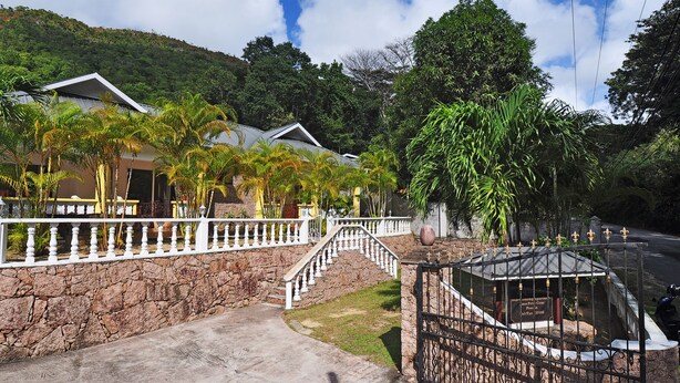 A residential area with a stone wall, white railings, and a gated entrance. - Acquario Villa (Praslin Island)