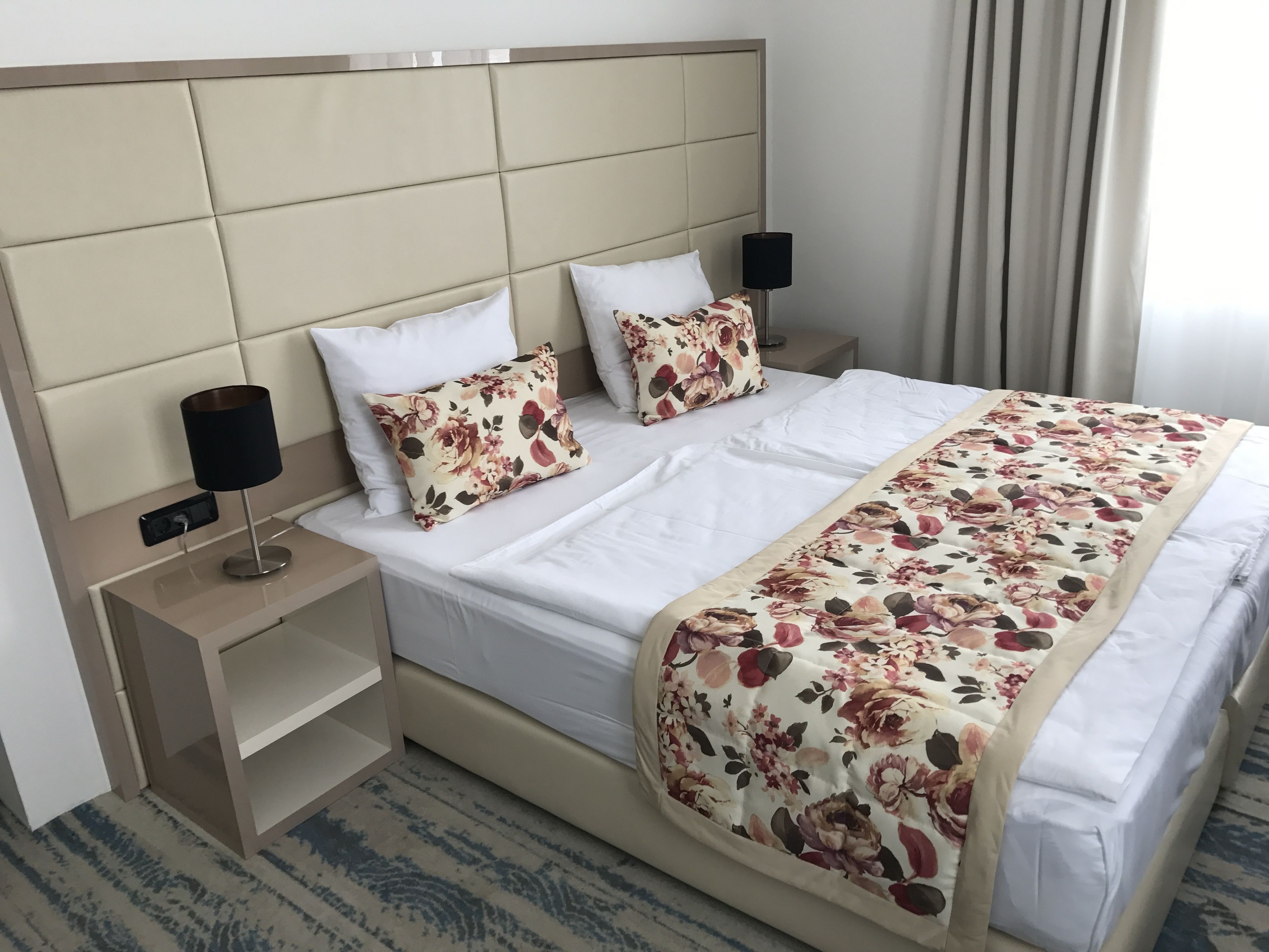 Habitación de hotel con una cama grande, dos mesitas de noche, una lámpara y un ventanal con cortinas.