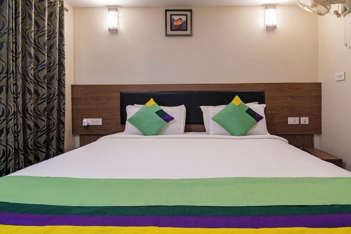 A hotel room with a large bed, two nightstands, a headboard, and a window with curtains.
