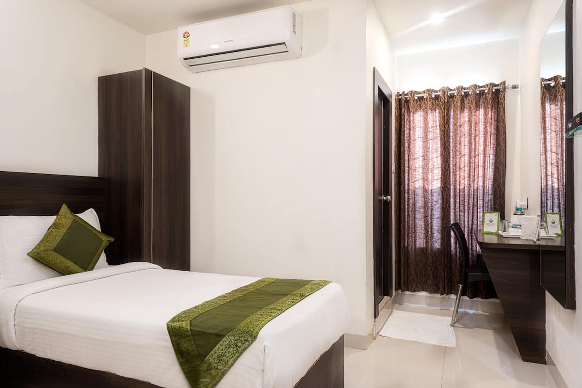 A hotel room with a bed, a wardrobe, an air conditioning unit, a desk with a chair, and a curtain.