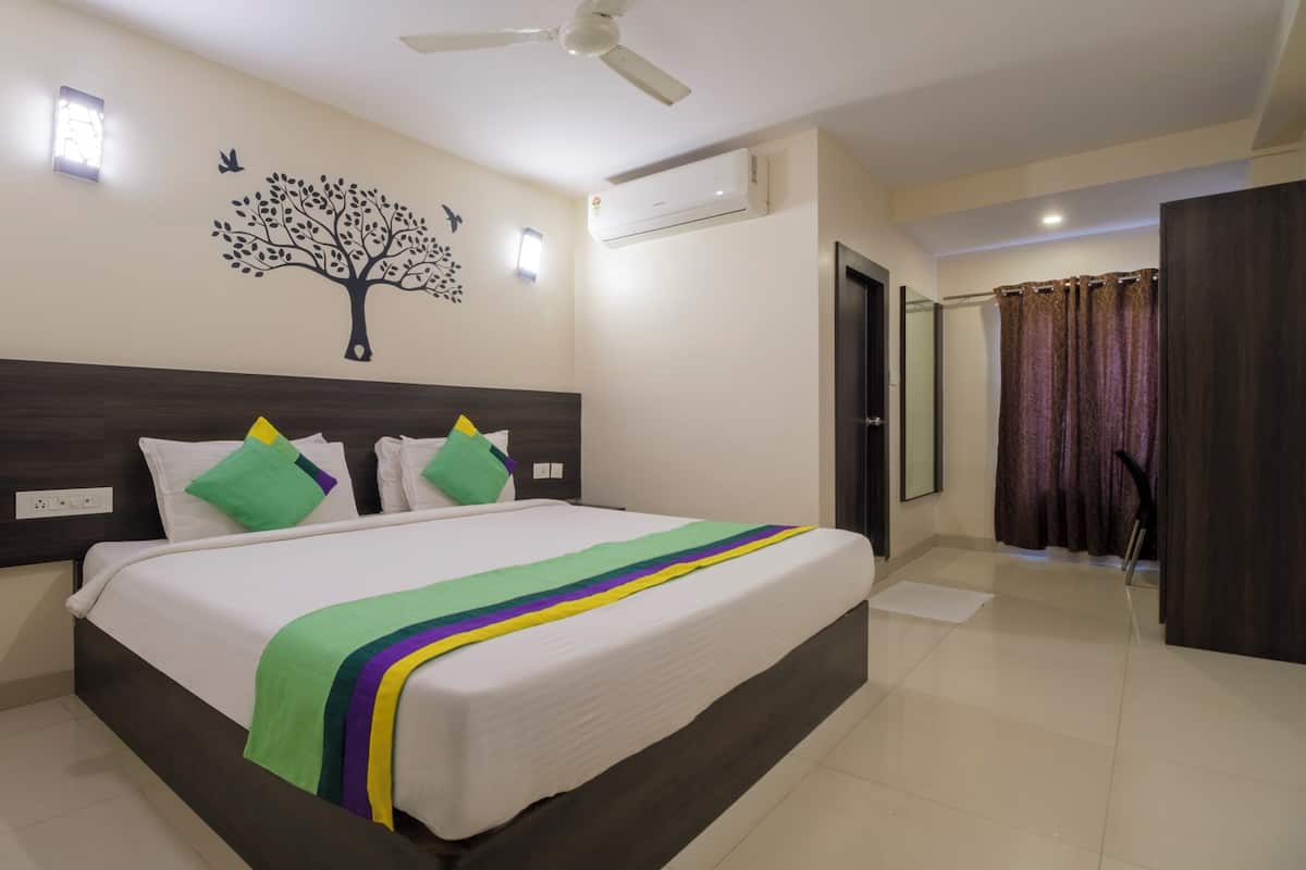 A hotel room with a large bed, a ceiling fan, an air conditioning unit, a wall-mounted light, and a door leading to a bathroom.