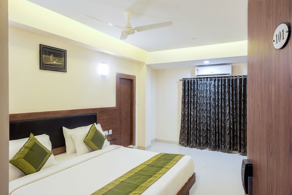 A hotel room with a bed, a ceiling fan, a framed picture on the wall, and a door.