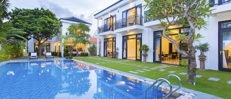 A modern house with a swimming pool, a well-maintained lawn, and a balcony with outdoor furniture.