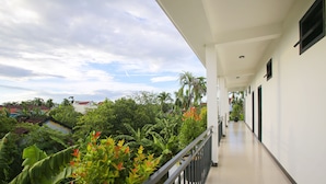 A long, narrow corridor with a balcony on one side, surrounded by lush greenery and a view of distant buildings. - Hoi An Hideaway Villa (Da Nang)