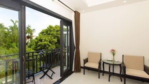 A balcony with a glass door, two chairs, a small table with a vase, and a view of greenery. - Hoi An Hideaway Villa (Da Nang)