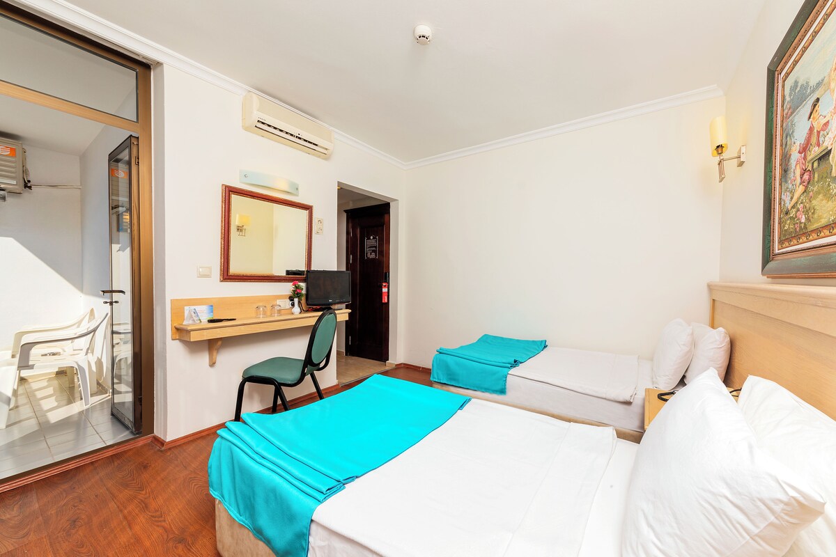 A hotel room with two beds, a desk with a chair, a mirror, and a door.