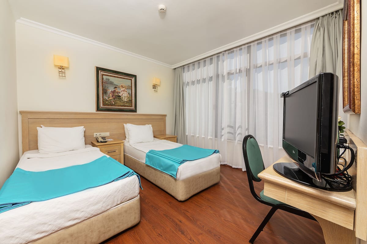 A hotel room with two beds, a desk with a computer, a chair, a TV, and a window with curtains.
