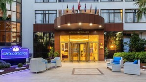 La entrada del Hotel Kayamaris, con puerta de vidrio, cartel y zona de estar al aire libre.