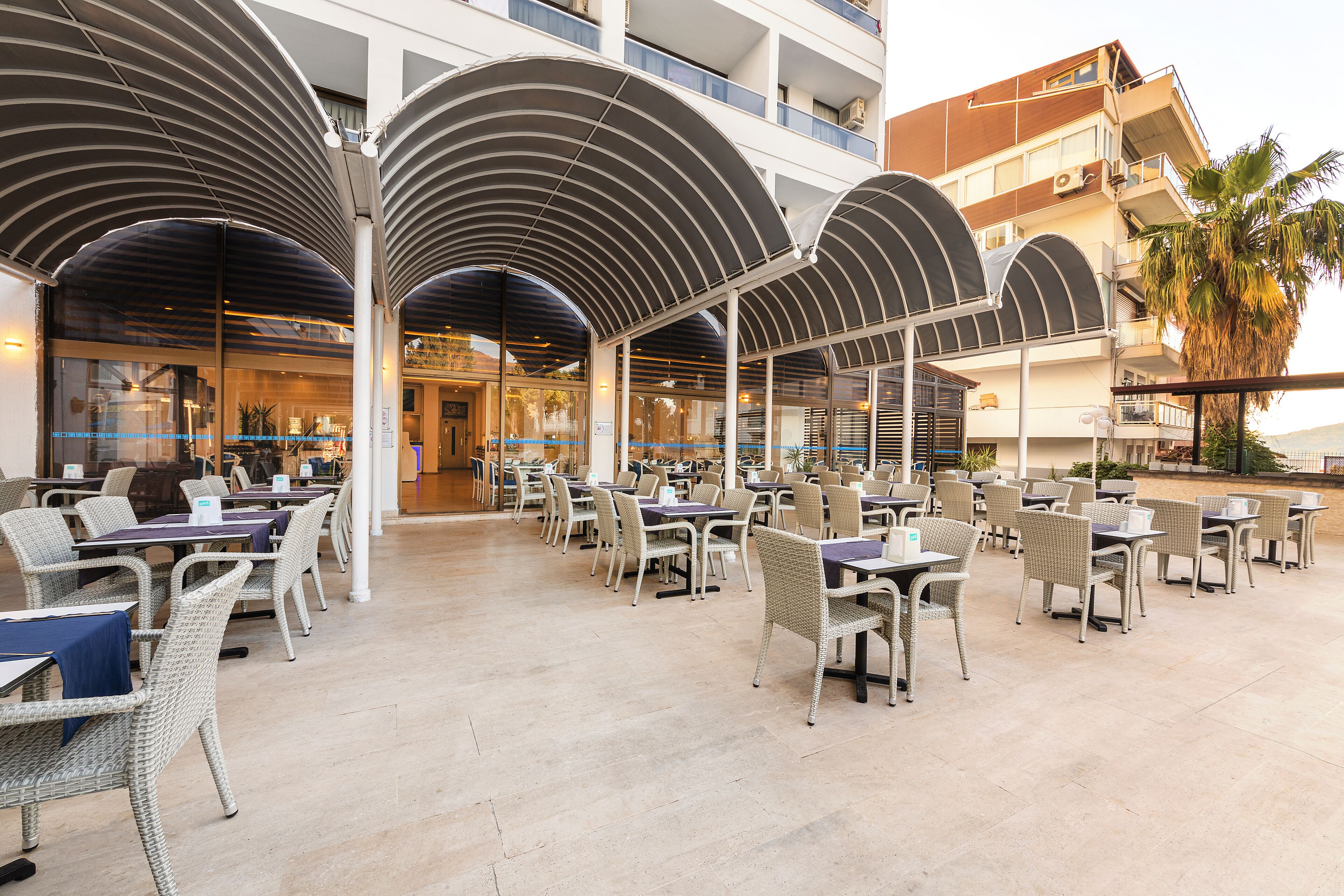 A spacious outdoor dining area with multiple tables and chairs, covered by large, curved canopies.
