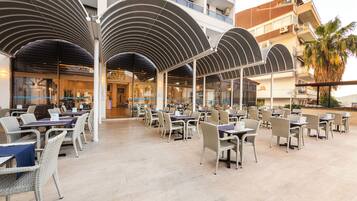 A spacious outdoor dining area with multiple tables and chairs, covered by large, curved canopies.