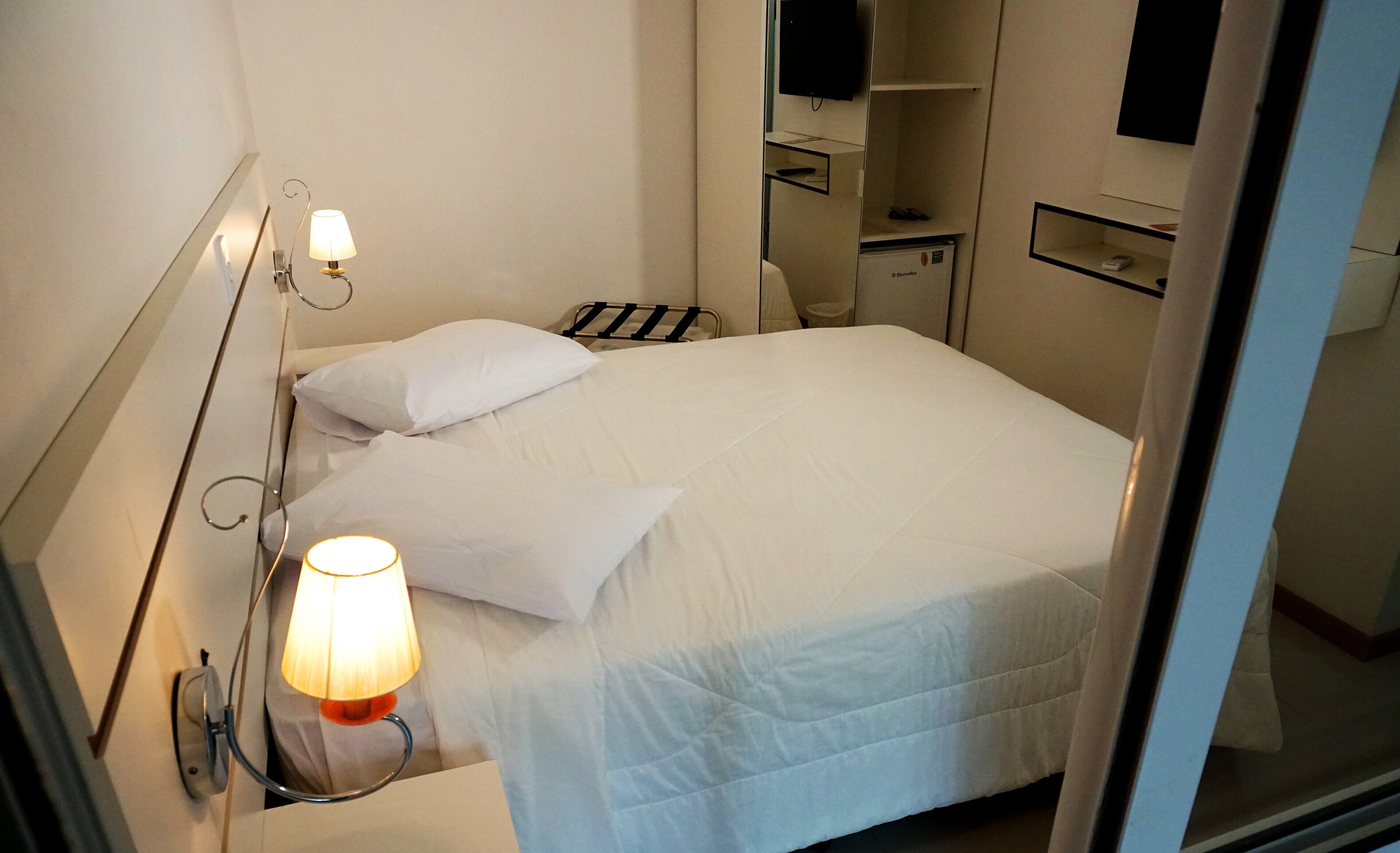 Ein Hotelzimmer mit Bett, Nachttischlampe, Fernseher und Minibar.