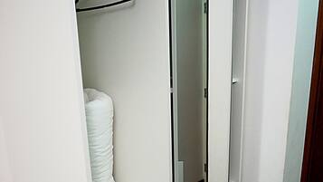 Een inloopkast met een spiegeldeur, planken met opgevouwen kleding en een kledingroede.