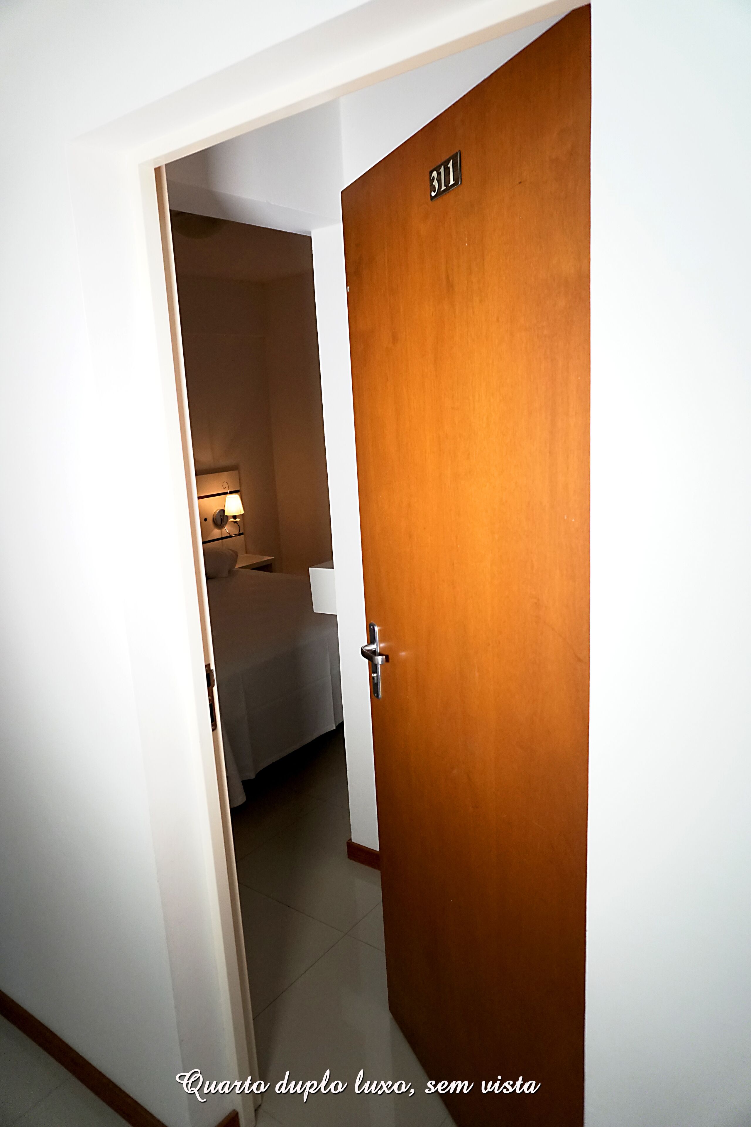 A hotel room with a wooden door, a bed, and a nightstand with a lamp. The room number is 311.