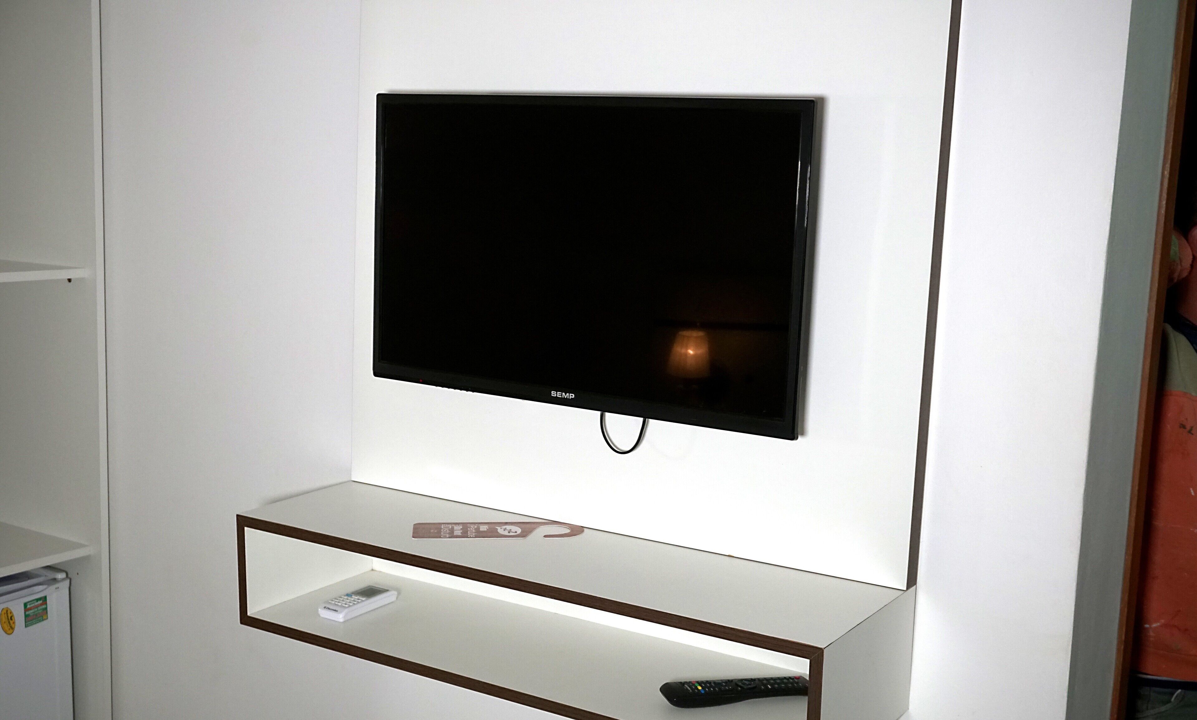 Een flatscreen televisie bevestigd aan een witte muur, met een klein plankje eronder.