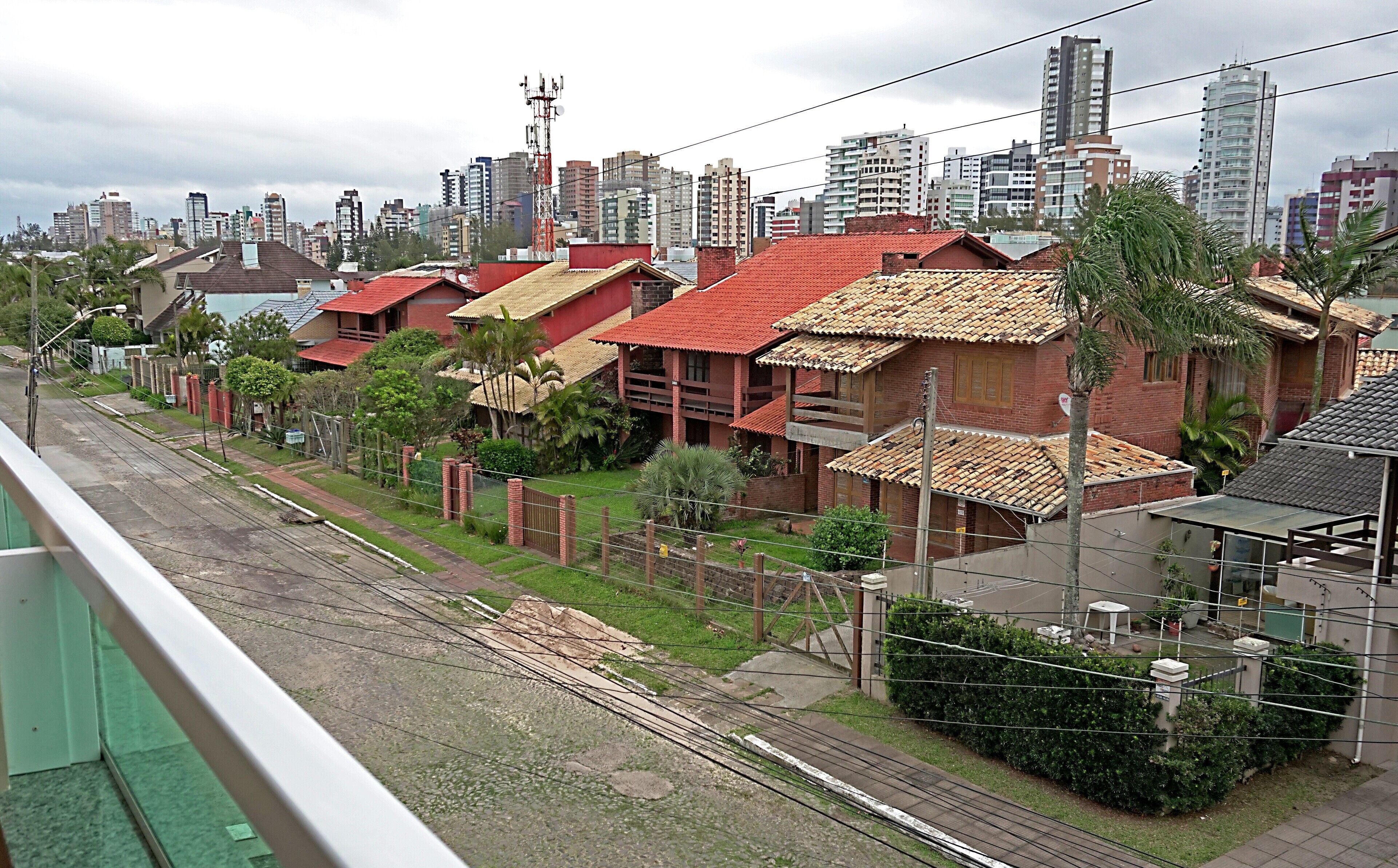 A residential area with houses featuring red-tiled roofs and brick construction, surrounded by a city skyline with high-rise buildings.
