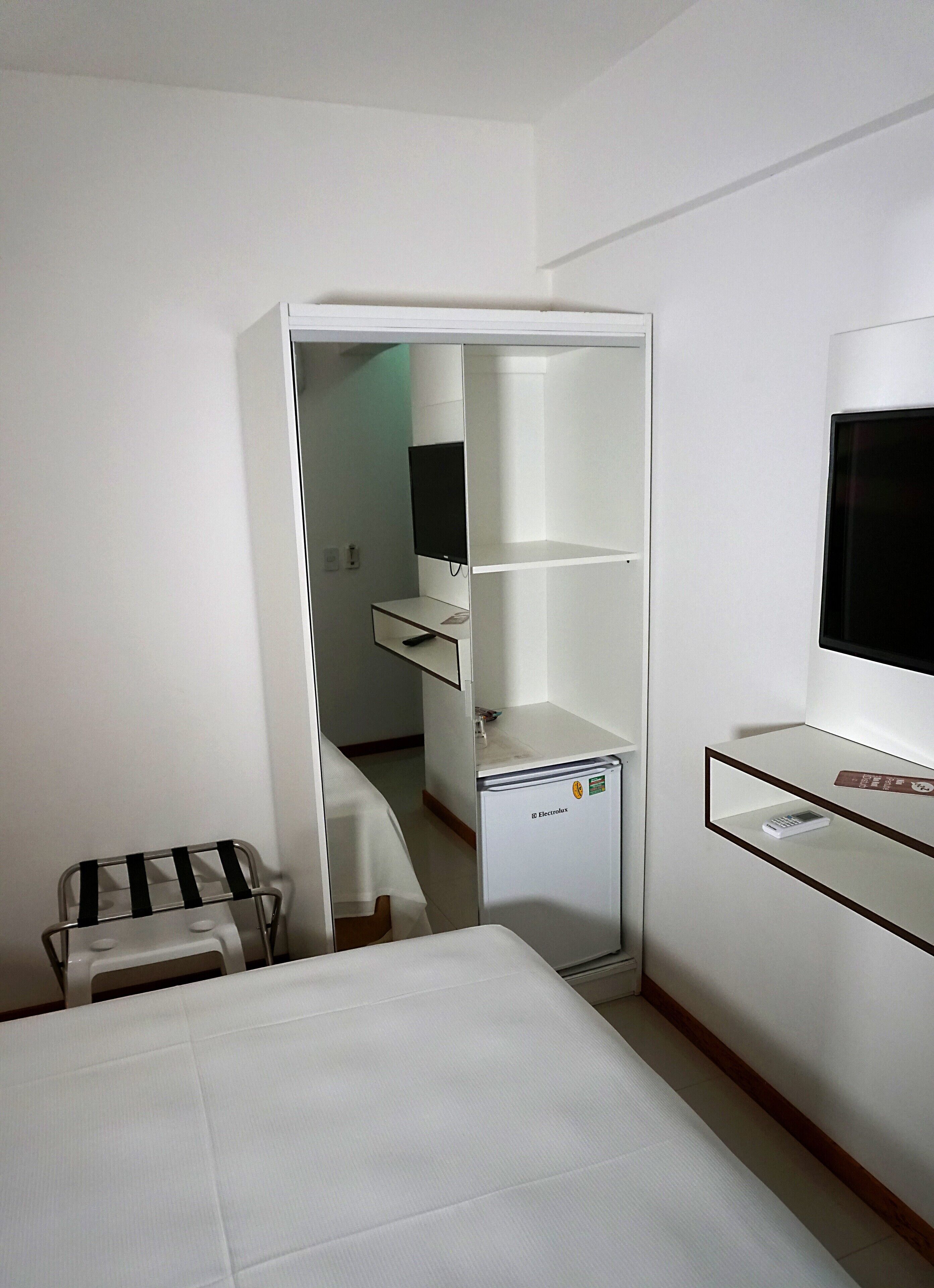 Una habitación de hotel con cama, minibar, televisor y escritorio.