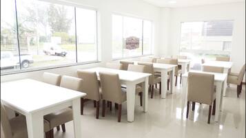 A bright, spacious dining area with white tables and chairs, large windows offering views of the street outside.