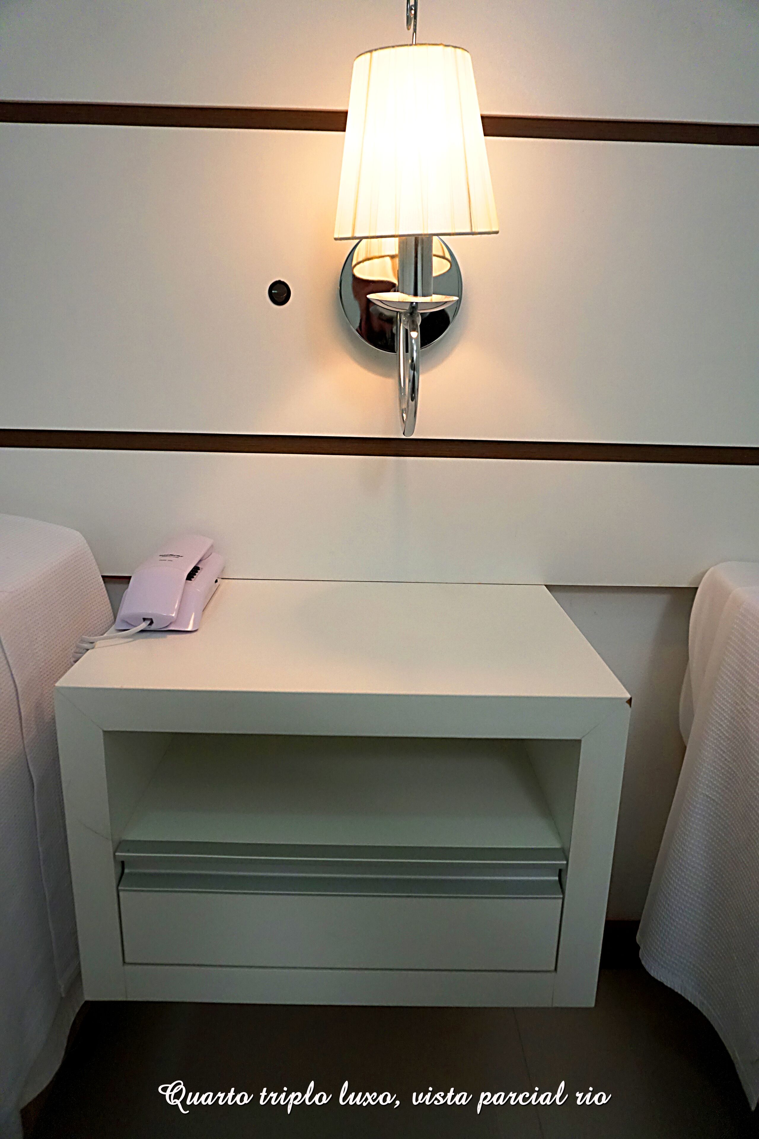 A hotel room with a bedside table, a lamp, and a phone.