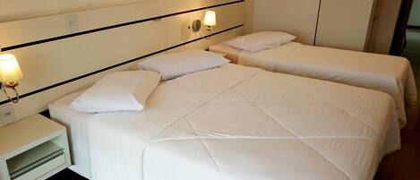 Una habitación de hotel con dos camas, una mesita de noche y una lámpara fijada a la pared.