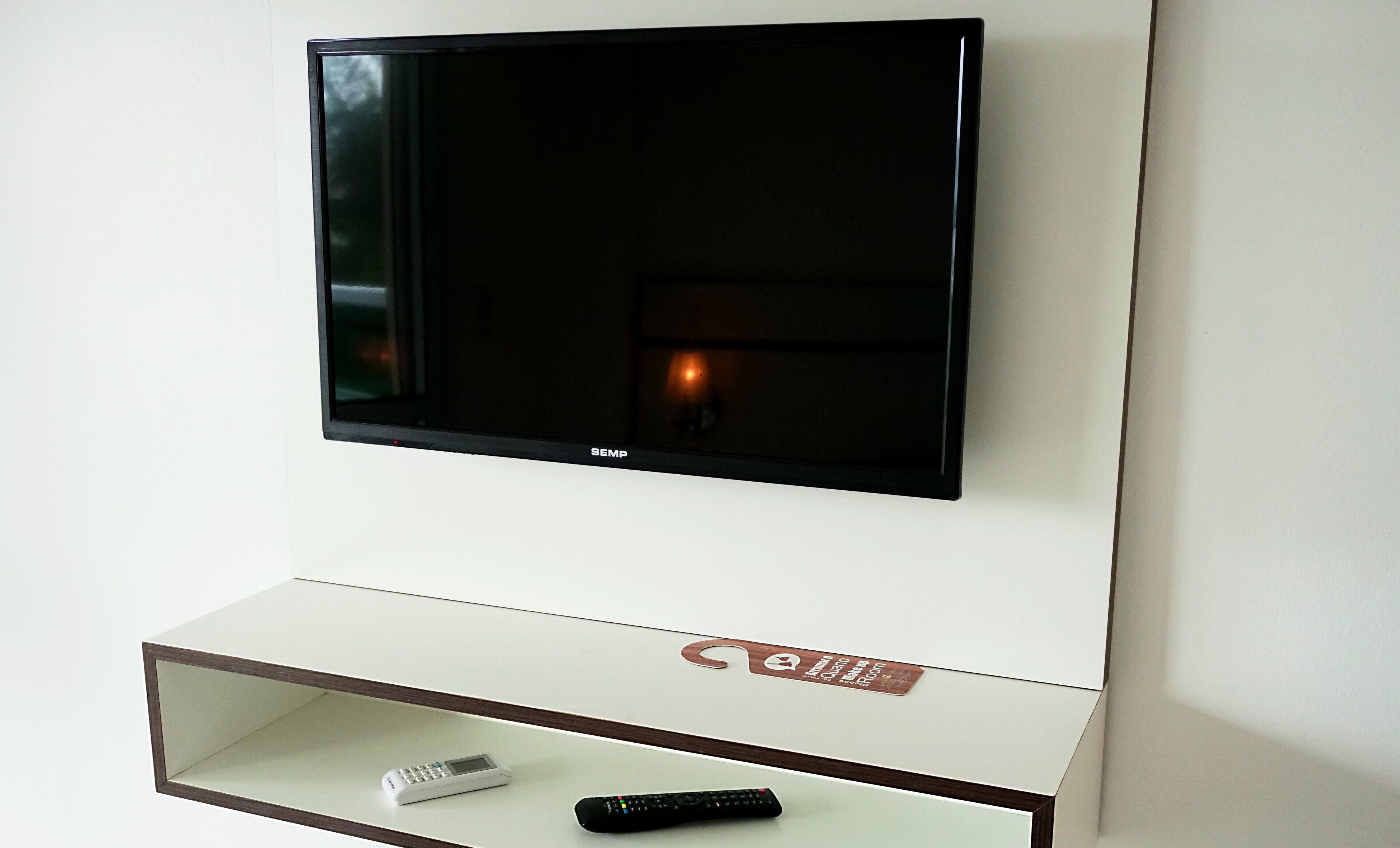 Televisor de pantalla plana montado en una pared con un estante blanco debajo.