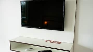 Televisor de pantalla plana montado en una pared con un estante blanco debajo.