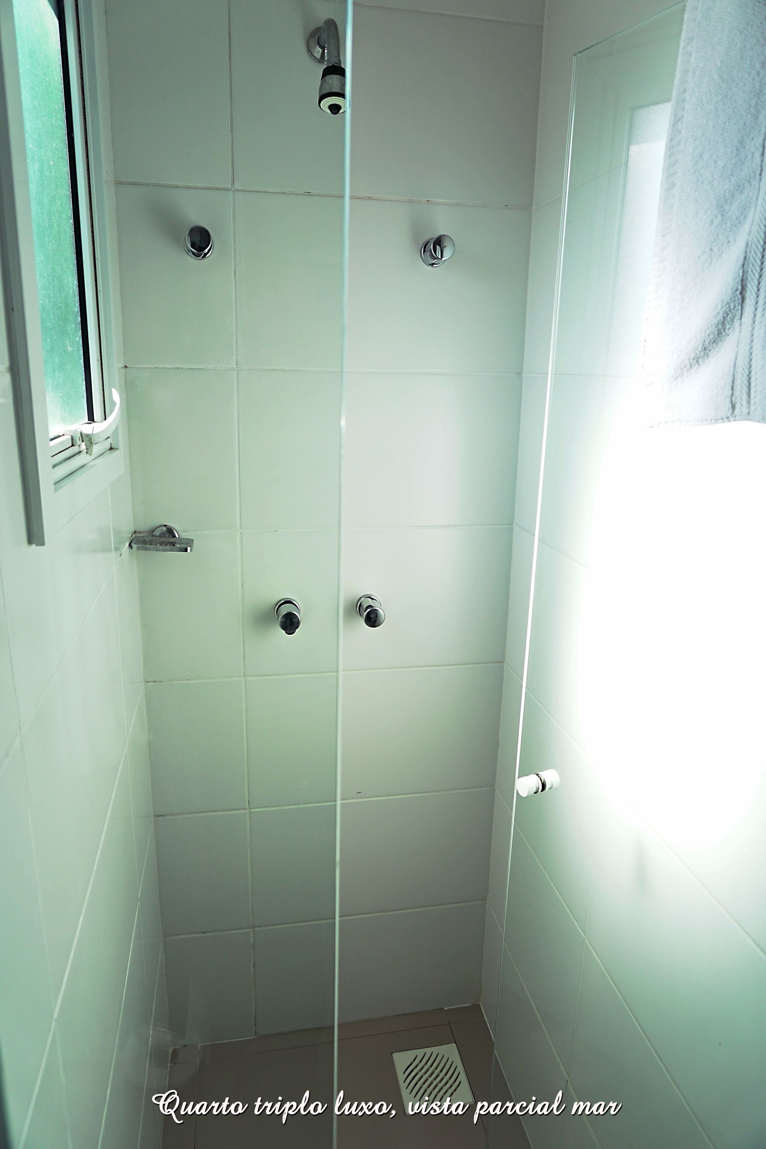 Un baño con azulejos blancos, ducha y ventana con una toalla colgada.