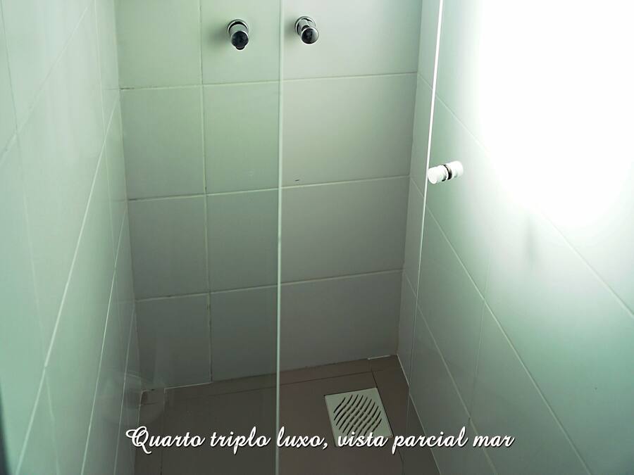 Un baño con azulejos blancos, ducha y ventana con una toalla colgada.