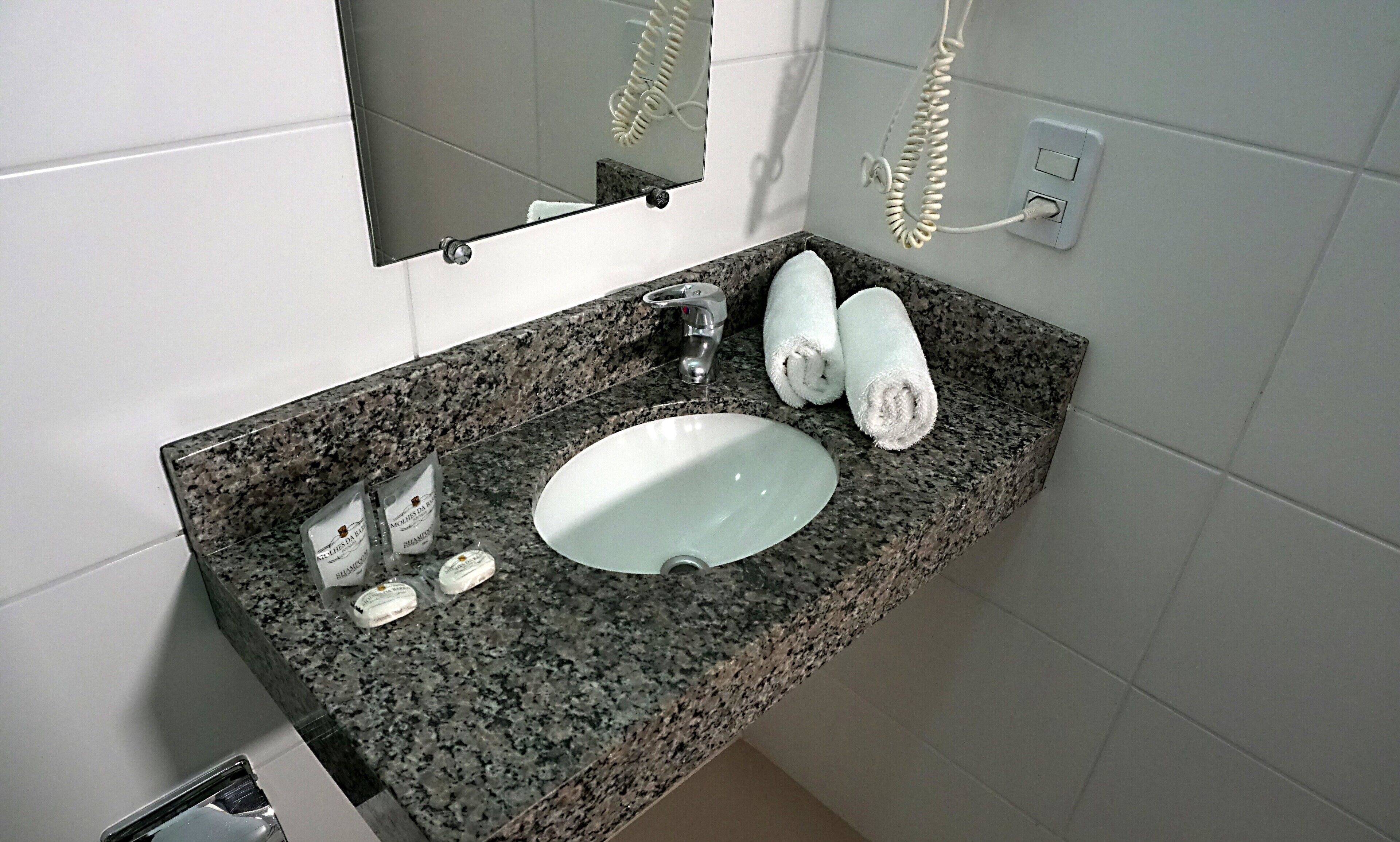 A bathroom with a granite countertop, a white sink, a mirror, a towel, and toiletries.
