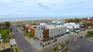 Un edificio residencial de varios pisos con balcones, vista a la calle y una playa al fondo.