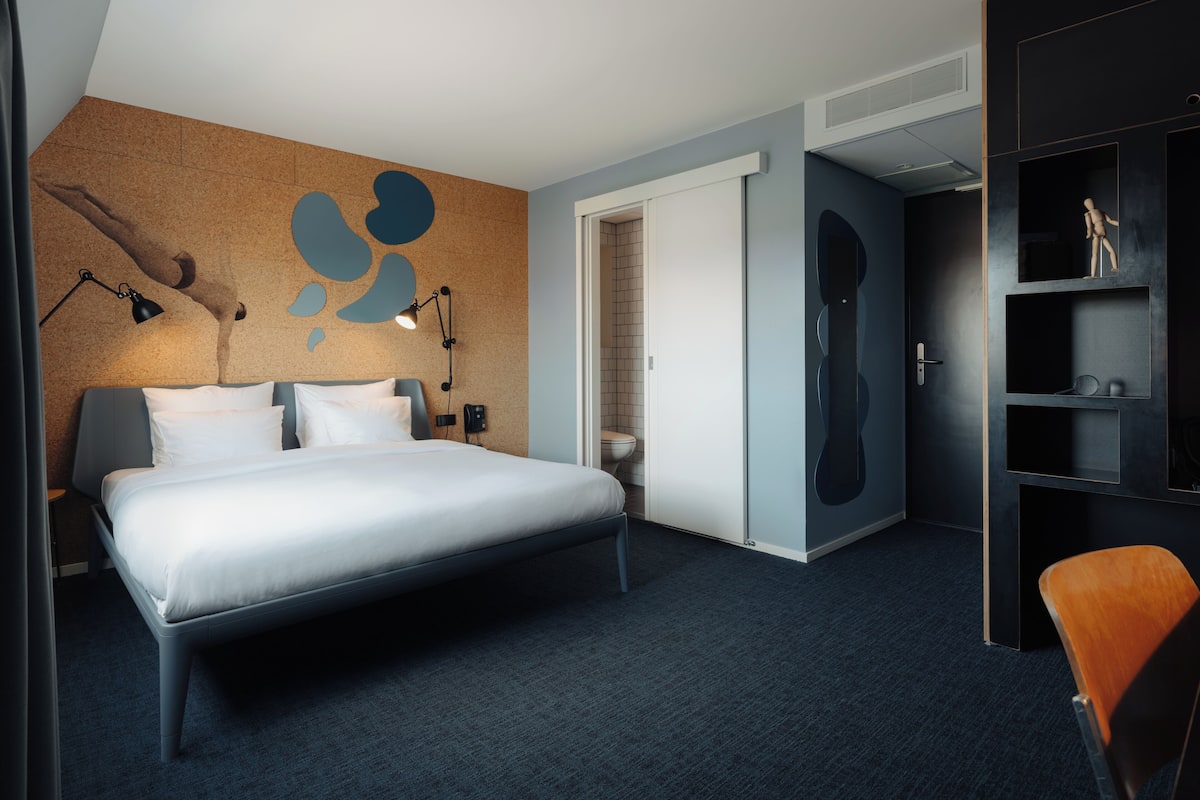 Quarto de hotel moderno com uma cama grande, uma escrivaninha, uma cadeira e um guarda-roupa.