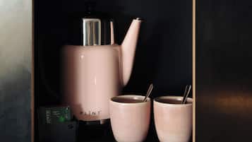 Un espositore nero con una macchina da caffè rosa, due tazze abbinate e una scatola con la scritta 'PLINT'.